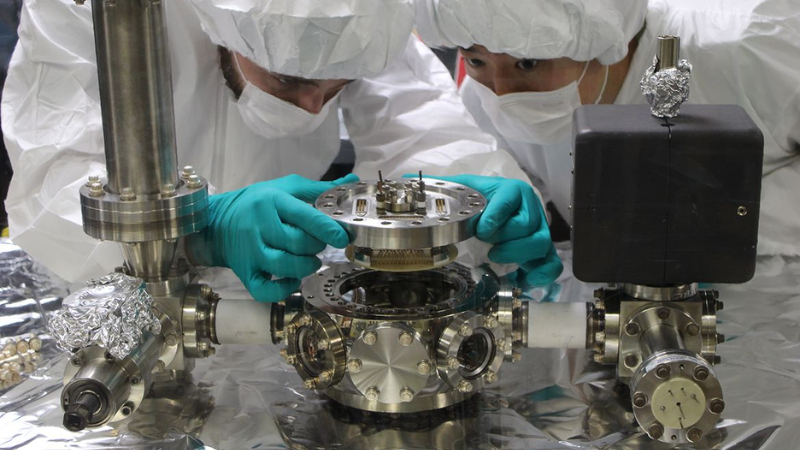 Graduate students Michael Bareian (UCLA, left) and Yiyang Zhi (UCB) carefully install the jointly developed integrated-photonics surface ion trap into the experimental vacuum system.